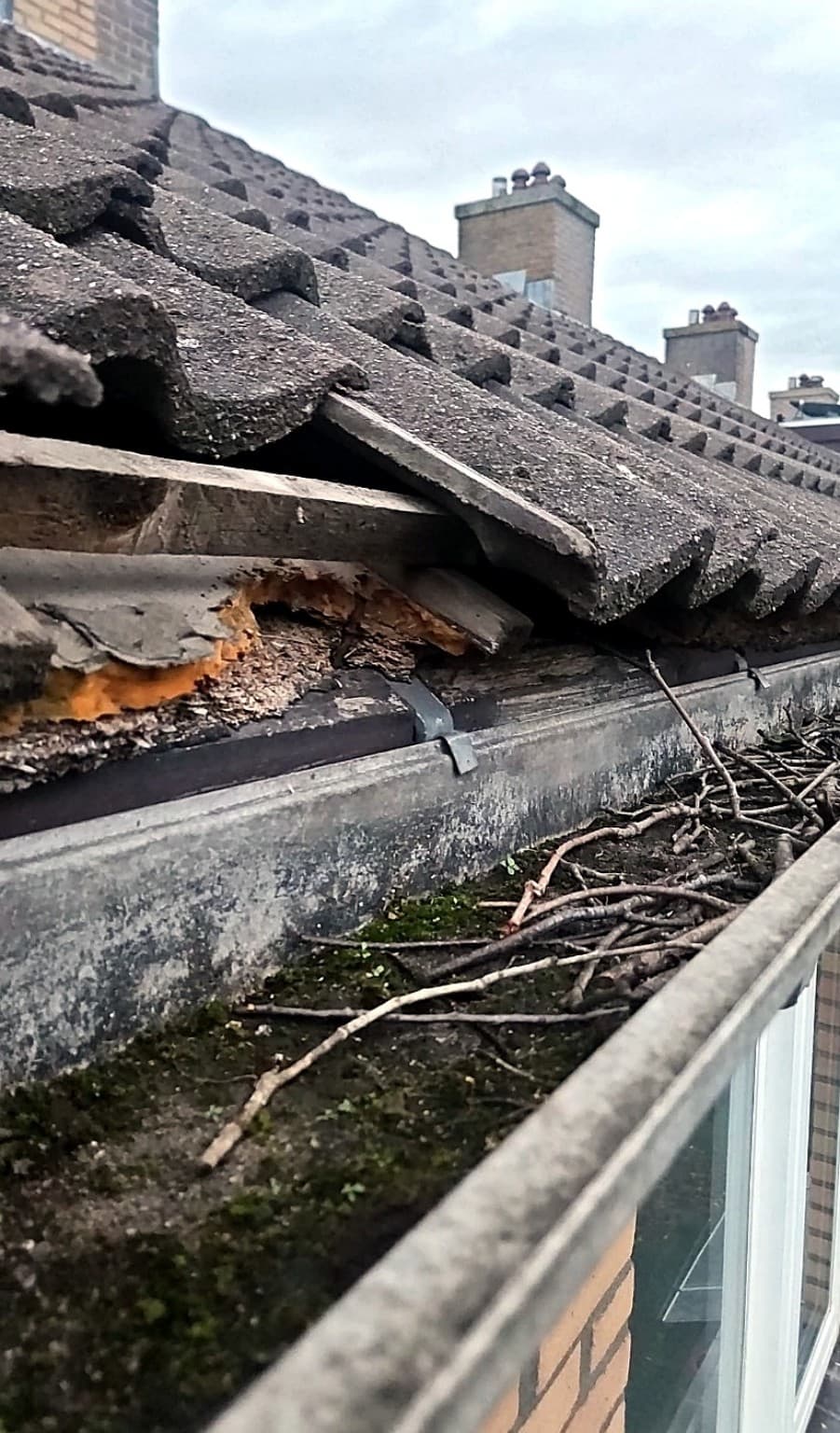 Beschadigde dakvoet met gebroken dakpannen en aangetast houtwerk